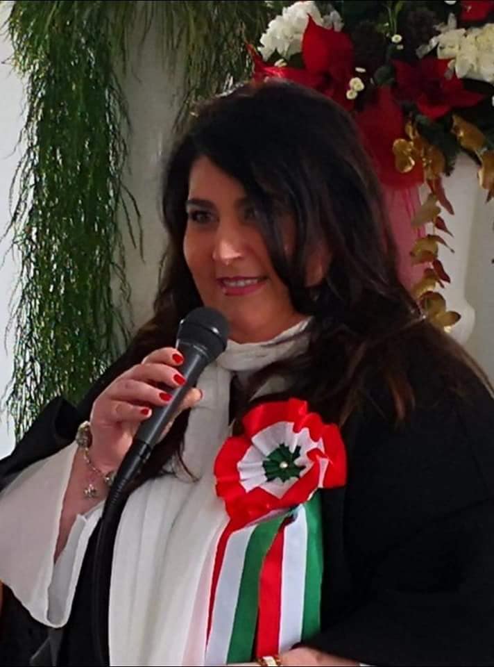 Ritratto di Claudia Vitrani al microfono durante una celebrazione, con coccarda tricolore